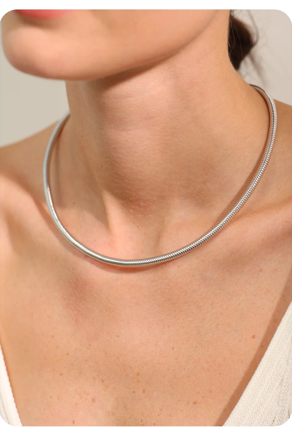 A stunning silver choker necklace elegantly wraps around the woman's neck, highlighting its timeless and sophisticated design. The smooth, reflective surface of the jewelry adds a touch of luxury to any outfit.