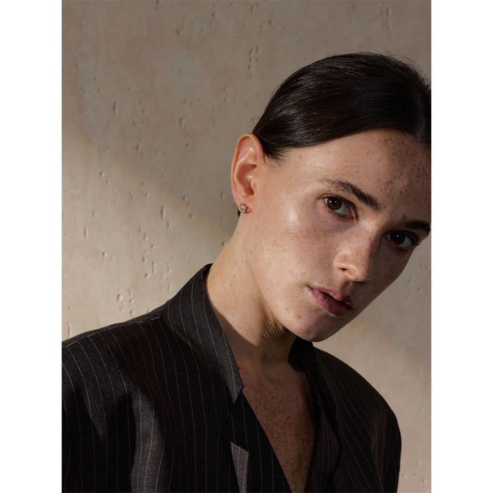 A close-up portrait highlighting delicate gold stud earrings adorned with sparkling gemstones. The timeless and elegant design adds a subtle touch of luxury, perfect for everyday wear or special occasions