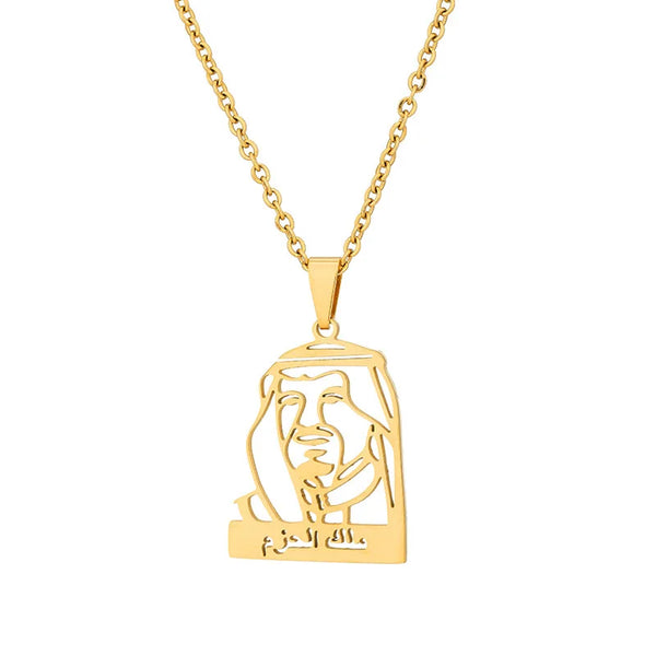 Close-up of a gold-tone pendant necklace depicting the stylized silhouette portrait of King Salman of Saudi Arabia. The Arabic inscription 'ملك الحزم' (Malik Al-Hazm, meaning 'King of Determination') is inscribed beneath the portrait. The necklace chain is visible.